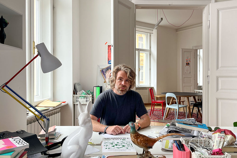 Martin Jenca, founder of Backstage Talks magazine, sits at his office desk surrounded by books and magazines.